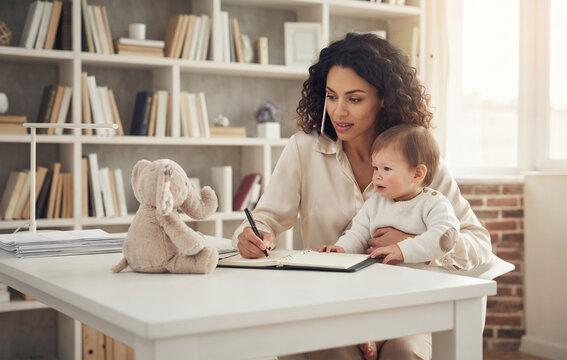 Working mother talking on phone and writing in planner while holding baby on lap at white desk in home office