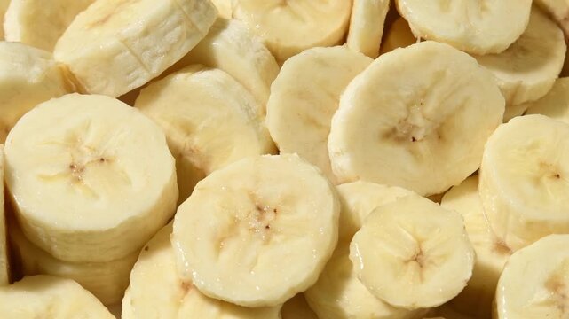 Overhead banana slices rotate in a horizontal frame, showing soft fruit texture and layered detail.