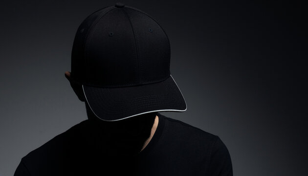 Front view blank black baseball cap mockup with white visor trim on man against dark studio background