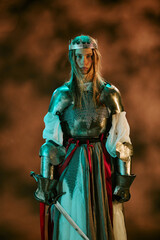 Obraz premium Portrait of young adult Caucasian woman wearing armor and crown holding sword representing leadership and strength. Media suitable for historical film promotion, gaming campaigns, vertical