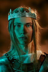 Obraz premium Portrait of young adult Caucasian woman wearing crown and armor, looking at camera. Concept of leadership, power and strength for gaming, fantasy book covers, vertical