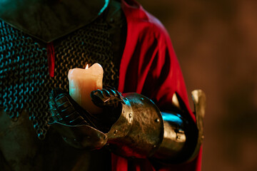 Obraz premium Medieval knight wearing metal armor gauntlet holding burning candle, representing hope and guidance. Useful for fantasy game promotion, book covers, and theatrical posters