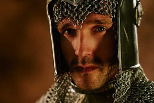 Portrait of young adult Caucasian man wearing chainmail helmet looking at camera with intense gaze. Image suitable for historical marketing, gaming concepts, close up