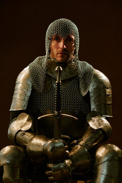 Portrait of young adult Caucasian man wearing medieval armor holding sword. Concept representing strength and protection for historical project or gaming branding, vertical