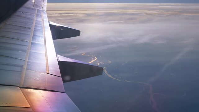 Commercial passenger airplane wing flying high above a winding river landscape and light clouds during a sunset flight. Beautiful scenic natural background template for global travel, international. 