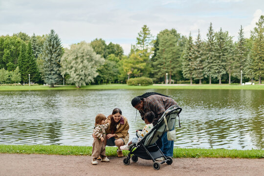 African American and Caucasian mothers spending time with toddler daughters near lake in public park. Multiethnic parenting concept suitable for family lifestyle advertising campaigns