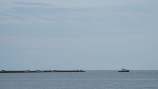 Colorful tugboat towing a small fishing boat with rope across calm blue sea, green navigation buoy and seagull on horizon