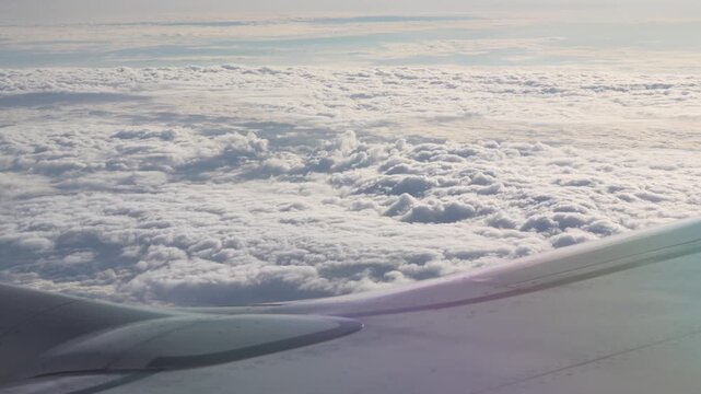 Commercial passenger airplane wing flying high above thick white cumulus clouds in a bright blue sky during a daytime flight. Beautiful heavenly natural landscape background template global travel. 