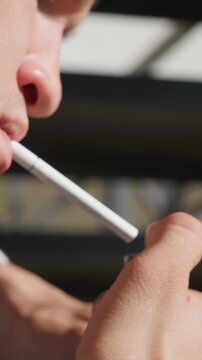 Close up of person using electronic cigarette indoors. person holds device near their mouth with soft lighting and shallow depth of field emphasizing hand texture and object detail