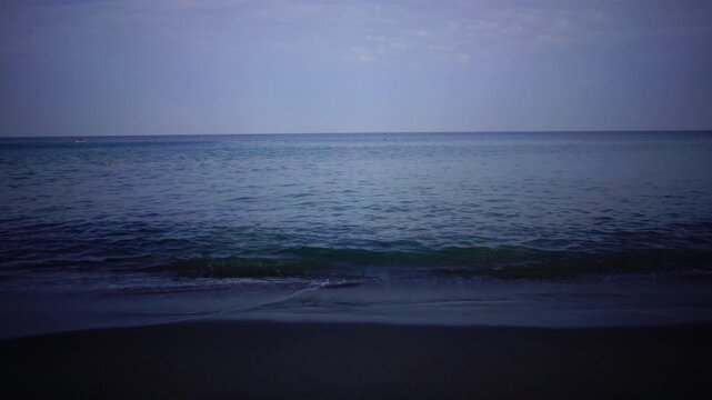 Calm ocean waves washing ashore on a sandy beach during dusk, serene sea horizon background footage