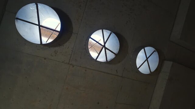 Concrete ceiling features circular vents reinforced with steel bars. Raw construction design highlights architectural utility features