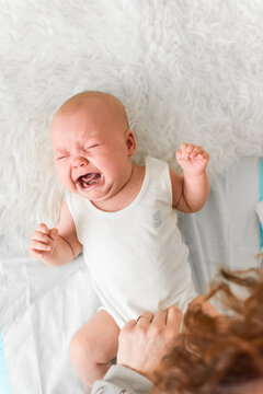 Baby 5-6 months old cries at home during care, emotional portrait with a natural expression of discomfort