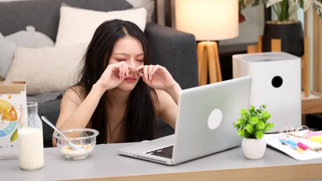 Tired Asian Woman Rubbing Eyes While Working on Laptop at Home