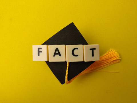 Letter tiles spelling FACT are placed over a miniature black graduation cap with a yellow tassel against a yellow background
