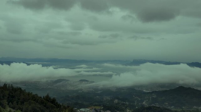 Sea of clouds rolling over mountain valley under cloudy sky