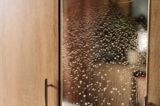 Foam droplets running down a wardrobe mirror beside wooden doors.
