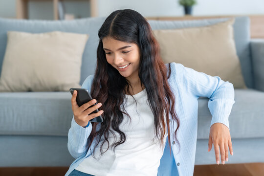 Smiling pretty young Asian woman sitting on the floor, using funny mobile apps in living room. Woman at Home, Doing Online Shopping, Messaging Friends, Posting on Social Media