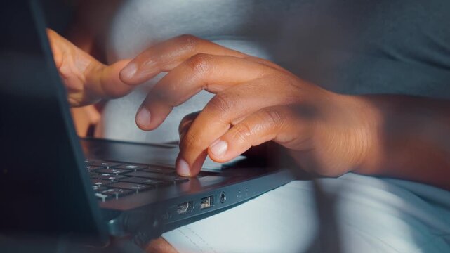 Close up view of hands typing on a laptop computer keyboard while working from bed
