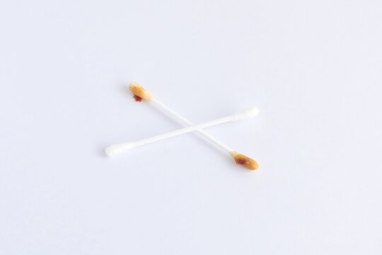 Crossed clean and dirty cotton swabs with ear wax on white background