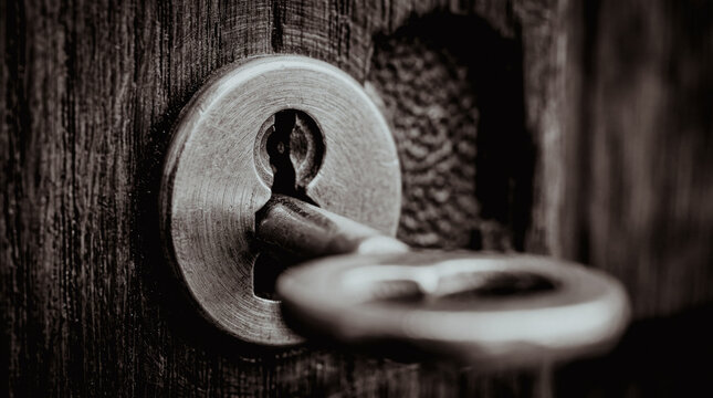 Old metal key inserted in a wooden door lock
