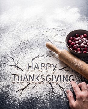 Happy Thanksgiving written in white flour on a dark rustic surface with rolling pin and cranberries