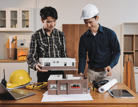 Asian architect and engineer team checking architectural house model using measuring tape on the table at office studio.
