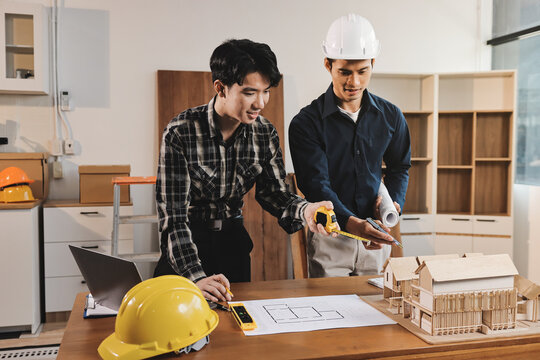 Asian architect and engineer team checking architectural house model using measuring tape on the table at office studio.