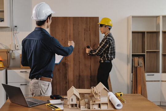 Asian architect and engineer team checking architectural house model using measuring tape on the table at office studio.