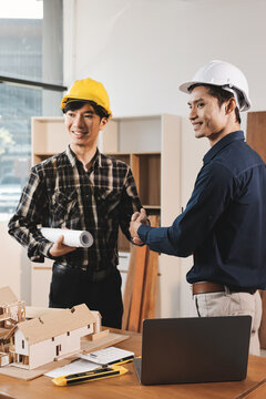 Asian architect and engineer team checking architectural house model using measuring tape on the table at office studio.