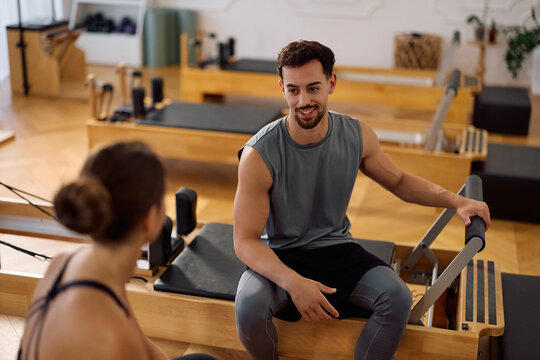 Happy athletic man and his friend communicating while taking break during Pilates training.
