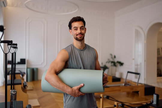 Smiling athlete with fitness mat in Pilates studio looking at camera.