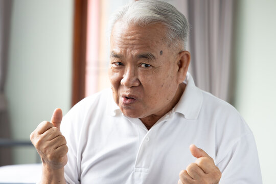 70s senior southeast asian man feeling excited and looking at camera at home, joyful expression in living room