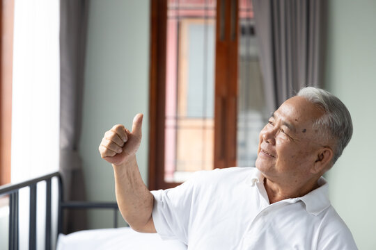 70s senior southeast asian man smiling and looking up with a happy expression, showing thumb up hand sign at home