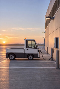 Electric airport utility vehicle charging beside building at sunset