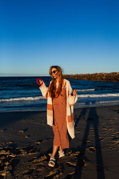 happy sunlit young woman at the beach with flying a kite holding onto reel with string to kite