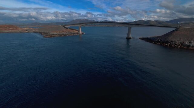 Aerial side view of the Atlantic Ocean Road in Norway in clear weather, showing the coastal route and bridge against the surrounding sea.