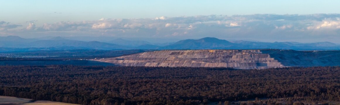 open cut coal mine on horizon in Hunter Valley seen over treetops from Bulga