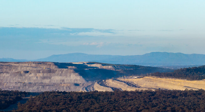 open cut coal mine on horizon in Hunter Valley seen over treetops from Bulga