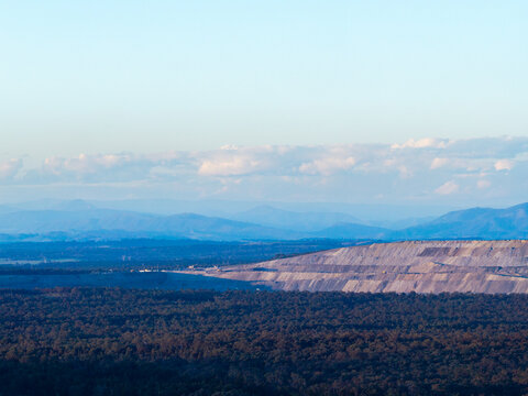 open cut coal mine on horizon in Hunter Valley seen over treetops from Bulga