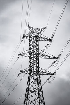 Tall electricity transmission tower and power lines silhouetted against a dramatic overcast sky, creating a stark industrial atmosphere with ample copy space