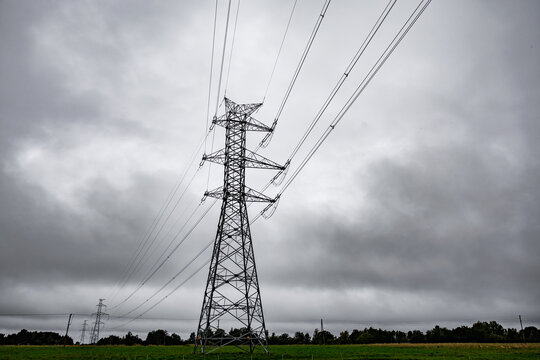 Tall electricity transmission tower and power lines silhouetted against a dramatic overcast sky, creating a stark industrial atmosphere with ample copy space