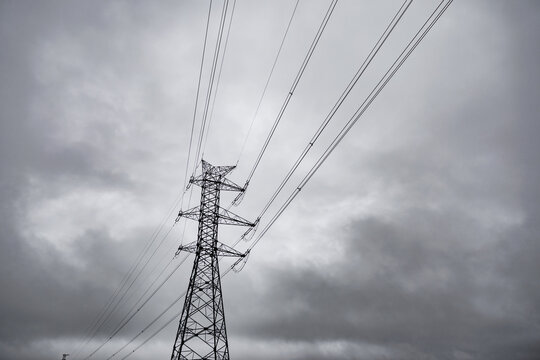 Tall electricity transmission tower and power lines silhouetted against a dramatic overcast sky, creating a stark industrial atmosphere with ample copy space