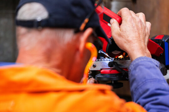 handyman in his fifties sharpening chainsaw teeth with electric sharpener tool in shed