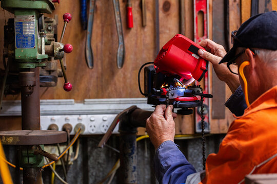handyman in his fifties sharpening chainsaw teeth with electric sharpener tool in shed
