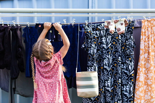 Young child reaching up helping hang out washing on outdoor line in backyard