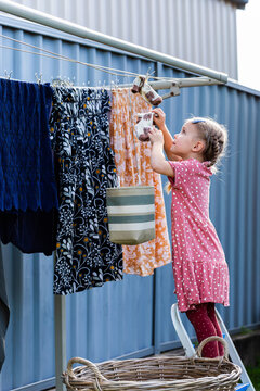 Young child on step stool helping hang out washing on outdoor line in backyard