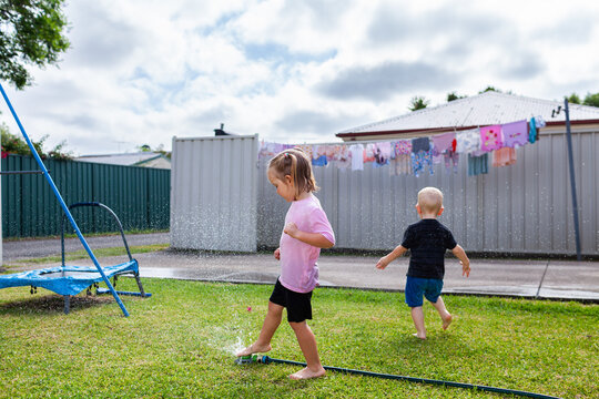 Children playing in backyard enjoying summertime fun with sprinkler and hose