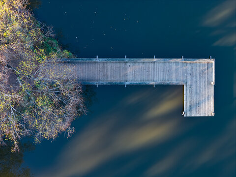 Aerial view of an empty wooden jetty over a calm lake covered in long shadows