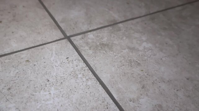Detailed camera movement gliding over a newly installed ceramic tile floor with dark gray grout lines, showing the texture and finish of the renovation work in a home interior