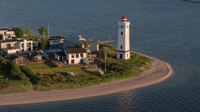 Aerial drone footage captures Strib Lighthouse surrounded by charming coastal houses along the Danish coastline near Middelfart, overlooking the calm waters of the Little Belt.